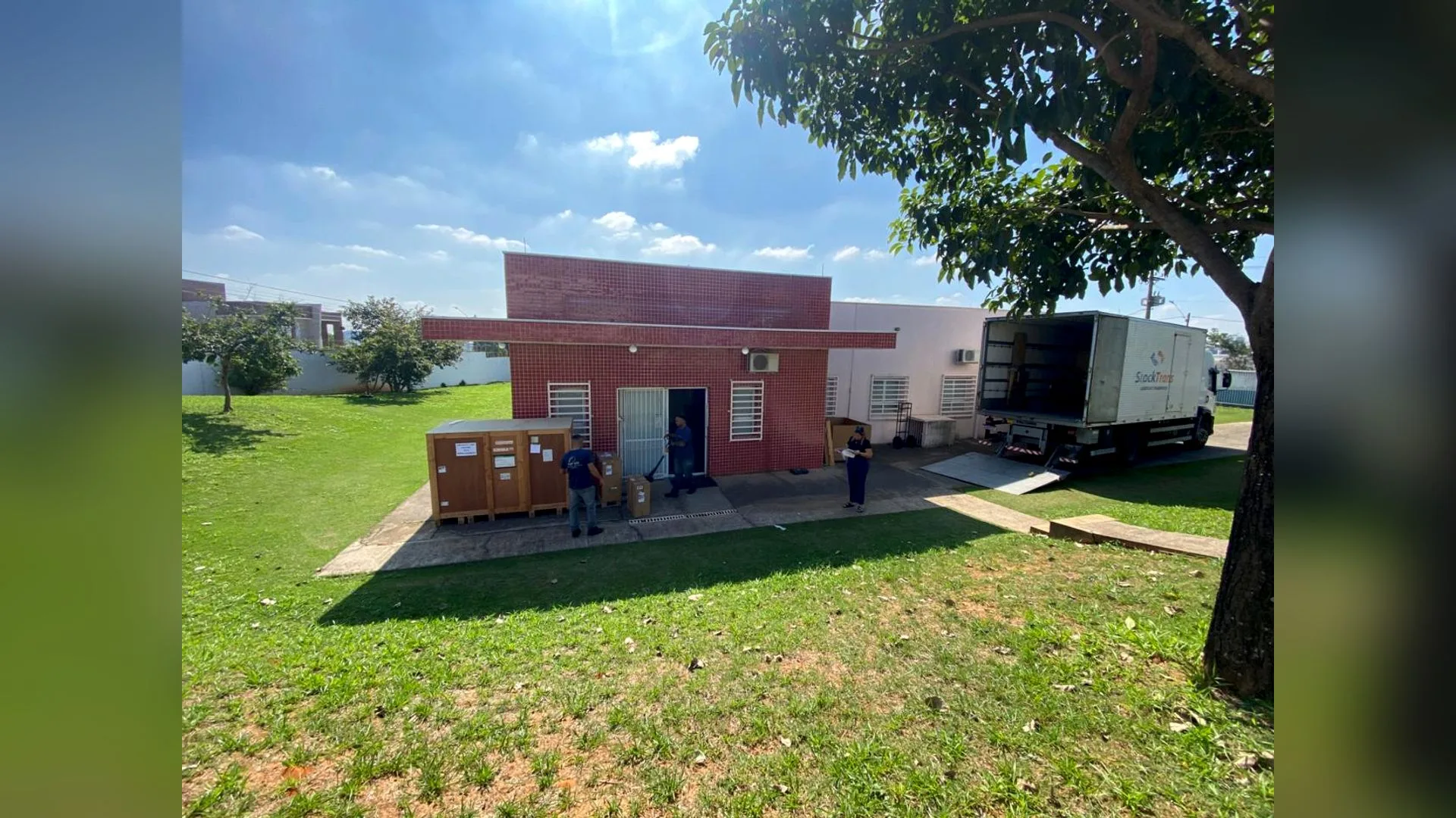 Vista externa do CAISM em Hortolândia, com caminhão de mudança descarregando caixas de madeira e funcionários.