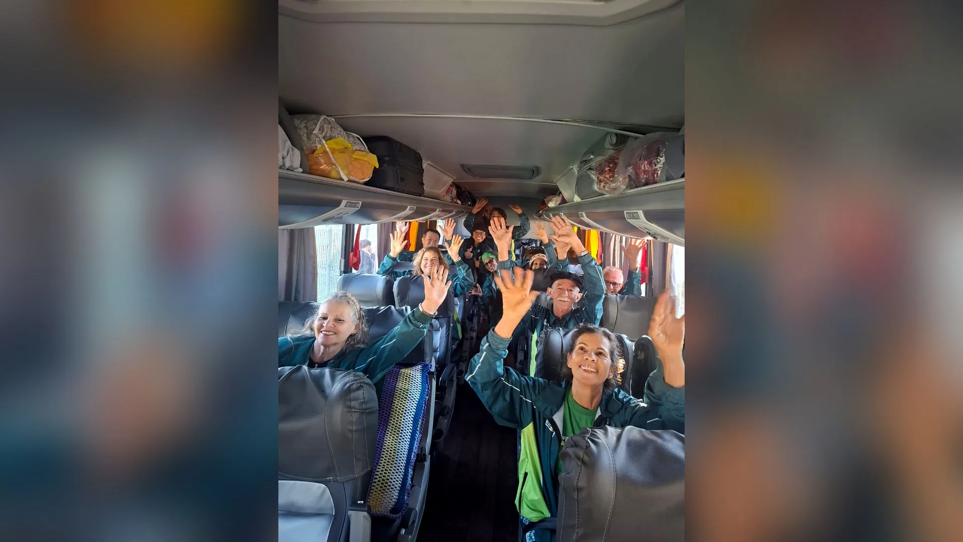 Atletas idosos de Sumaré sorriem e acenam dentro de um ônibus, prontos para embarcar nos Jogos da Melhor Idade.