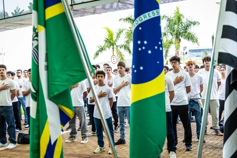 Jovens com braço estendido prestando compromisso cívico perante a Bandeira Nacional no Paço Municipal de Paulínia