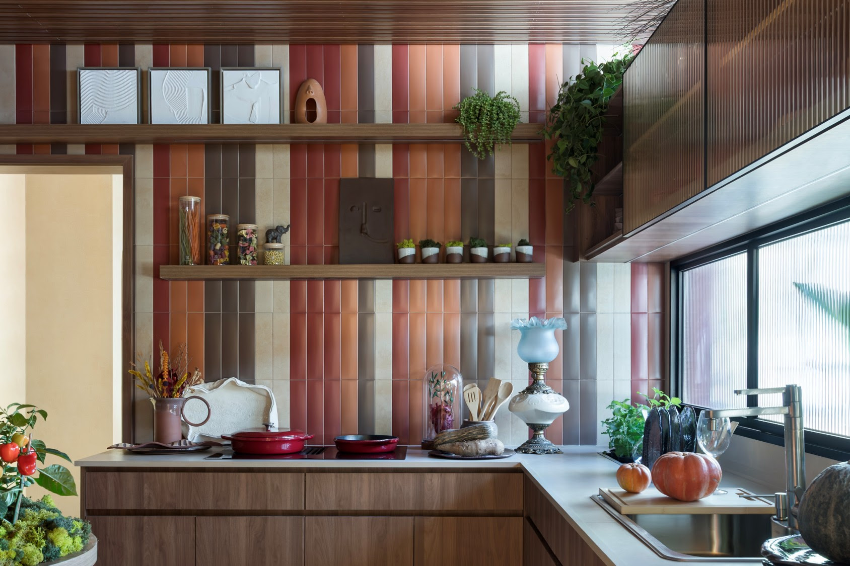 Cozinha moderna com revestimento cerâmico vertical em tons de terracota, prateleiras de madeira e vegetação natural