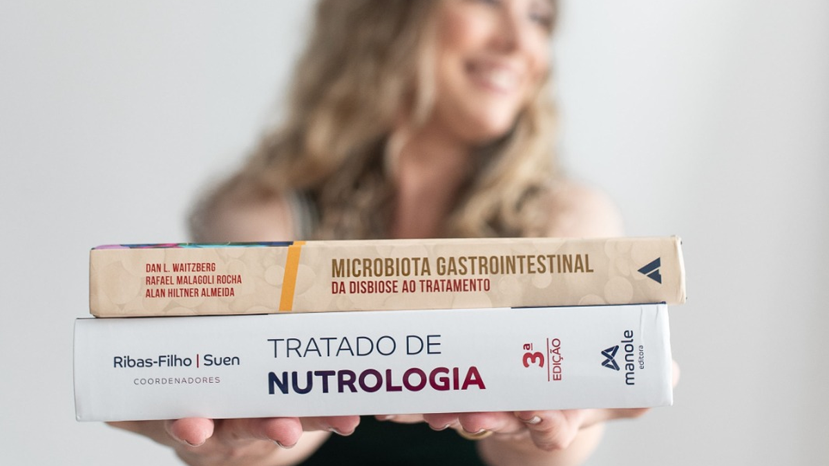 Profissional de saúde segurando livros de Tratado de Nutrologia e Microbiota Gastrointestinal