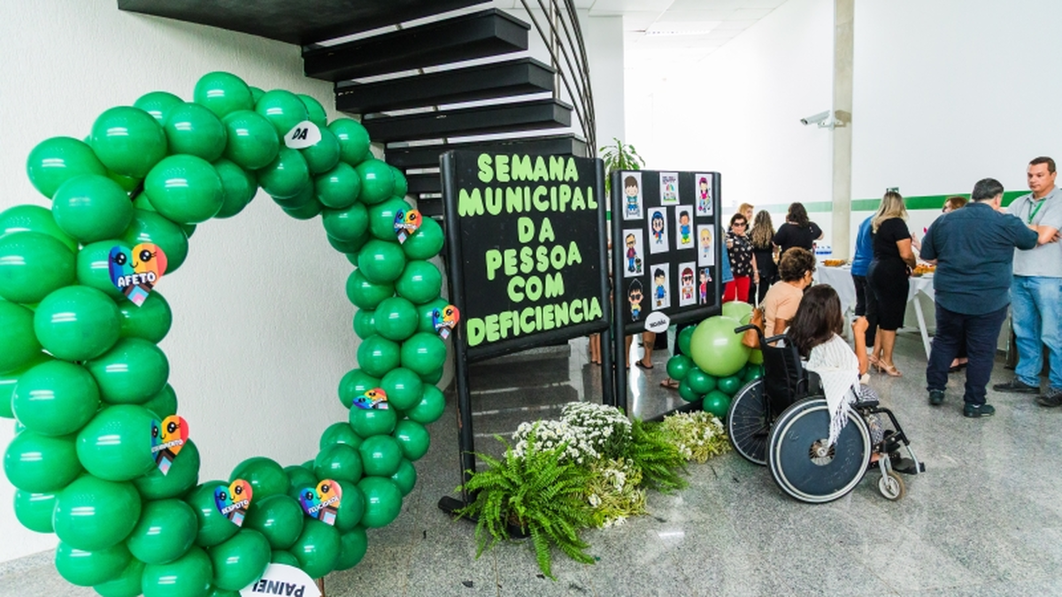 Espaço decorado com balões verdes e placa da Semana Municipal da Pessoa com Deficiência em Paulínia