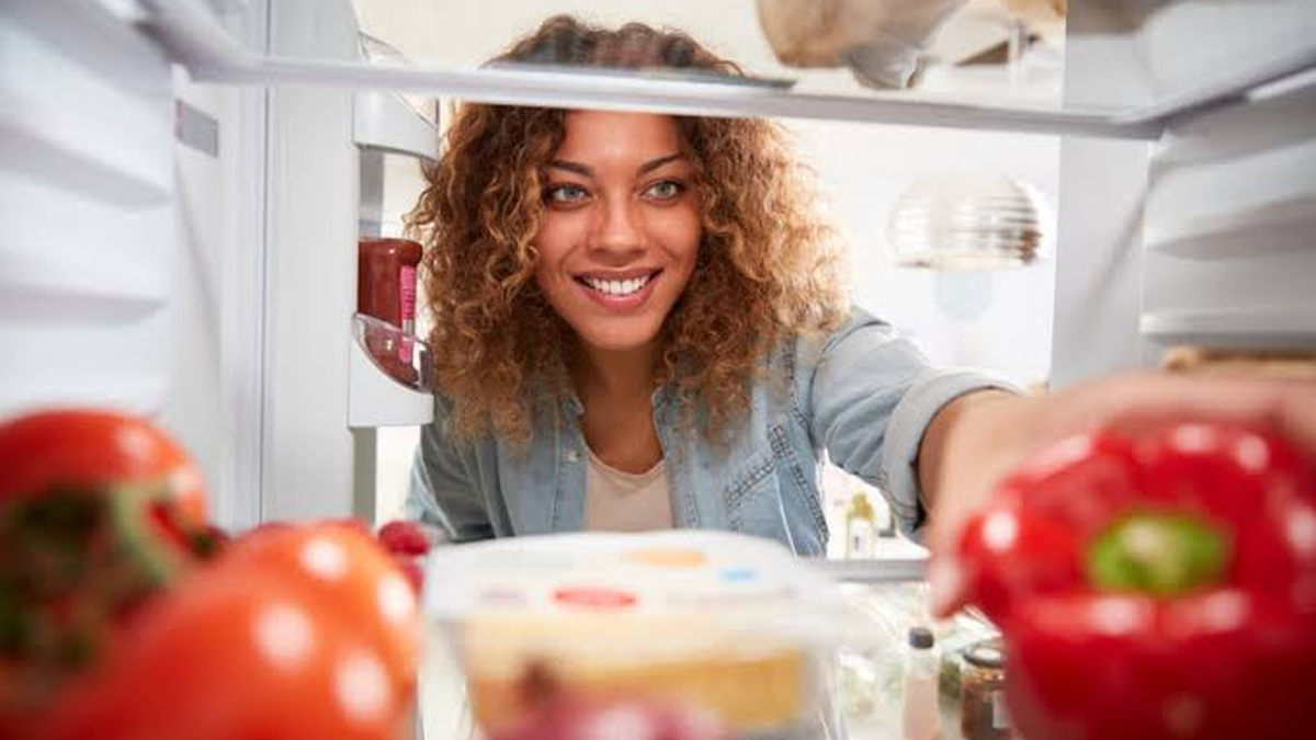 Mulher sorridente abrindo a geladeira para escolher alimentos frescos e vegetais