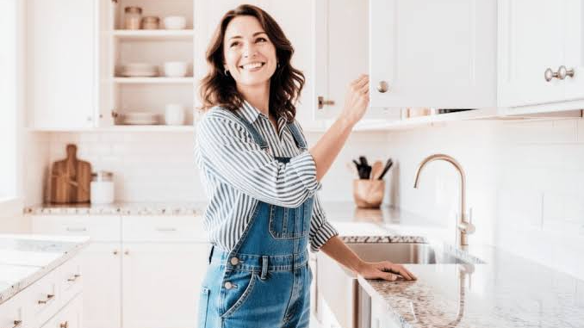 Mulher sorridente abrindo armário em cozinha organizada e iluminada