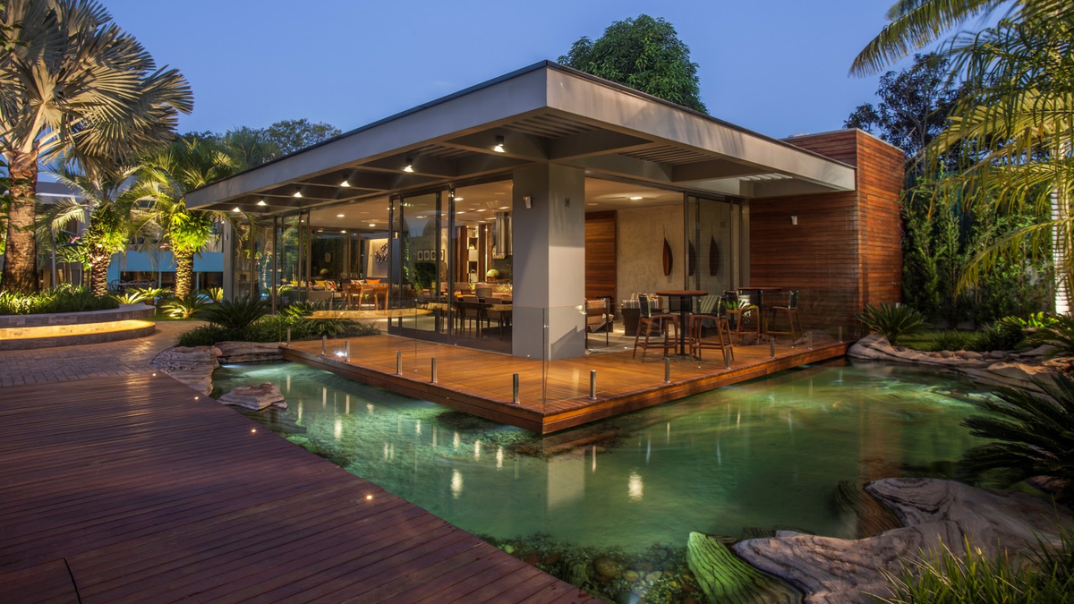 Lago natural com pedras e deck de madeira envolvendo espaço gourmet residencial iluminado