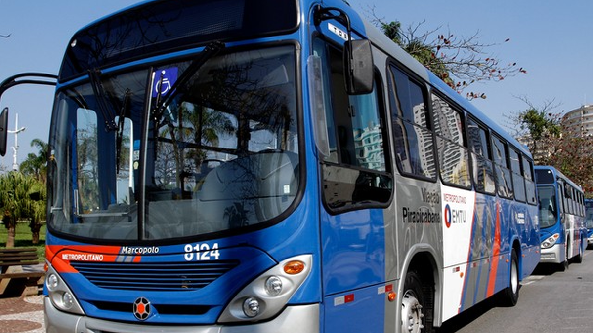 Ônibus metropolitano azul estacionado, com outro veículo ao fundo.