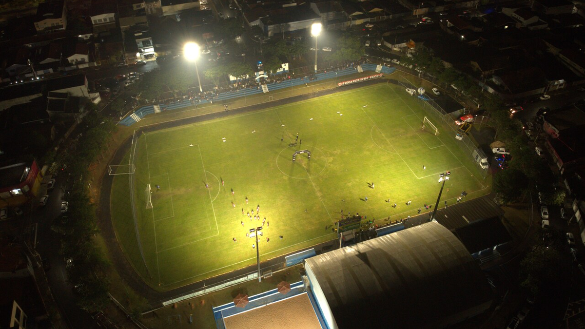 Vista aérea noturna de campo de futebol iluminado durante jogo amador em Hortolândia